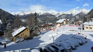 A snow-covered parking area with several cars, a building with a sloped roof, and a mountain range in the background. - Valfréjus – 6 people – Skiing & panoramic views (Modane)