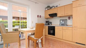 A kitchen with wooden cabinets, a dining table, chairs, and a view of a garden through a glass door. - Apartment 'Anna Nordsee' with Private Terrace, Private Garden and Wi-Fi (Krummhörn)