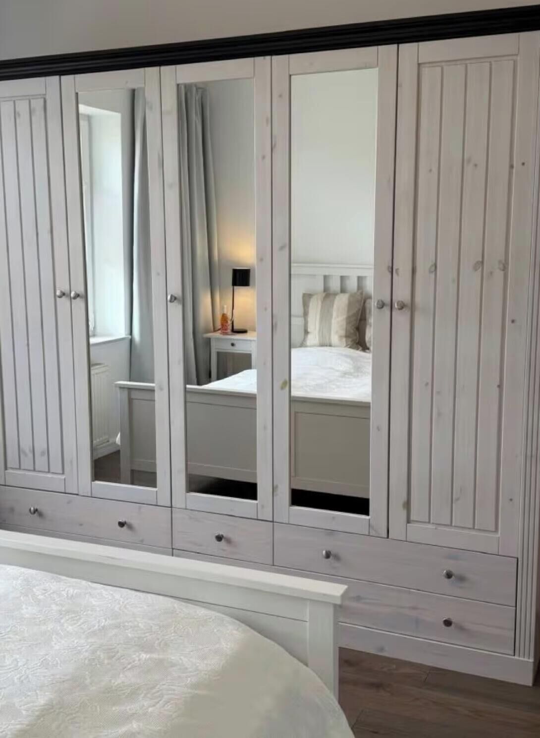 Ein Schlafzimmer mit großem Kleiderschrank, einem Bett und einem Nachttisch mit Lampe.