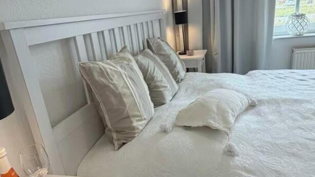 A hotel room with a bed, bedside table, lamp, and window with curtains. - Apartment 'Anna Nordsee' with Private Terrace, Private Garden and Wi-Fi (Krummhörn)