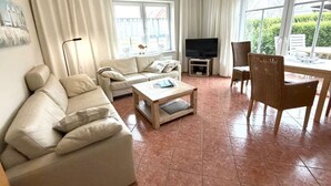 A living room with a sofa, a coffee table, a TV stand, and a dining area with a table and chairs. - Apartment 'Anna Nordsee' with Private Terrace, Private Garden and Wi-Fi (Krummhörn)