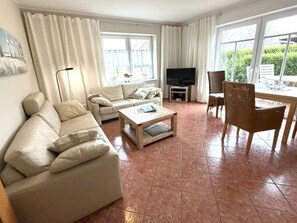 Ein Wohnzimmer mit einer Couch, einem Couchtisch, einer TV-Konsole und einem Essbereich mit Tisch und Stühlen.