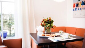Un comedor con una mesa dispuesta para el desayuno, que incluye pasteles y una taza de café, un jarrón de tulipanes y un cuadro en la pared.
