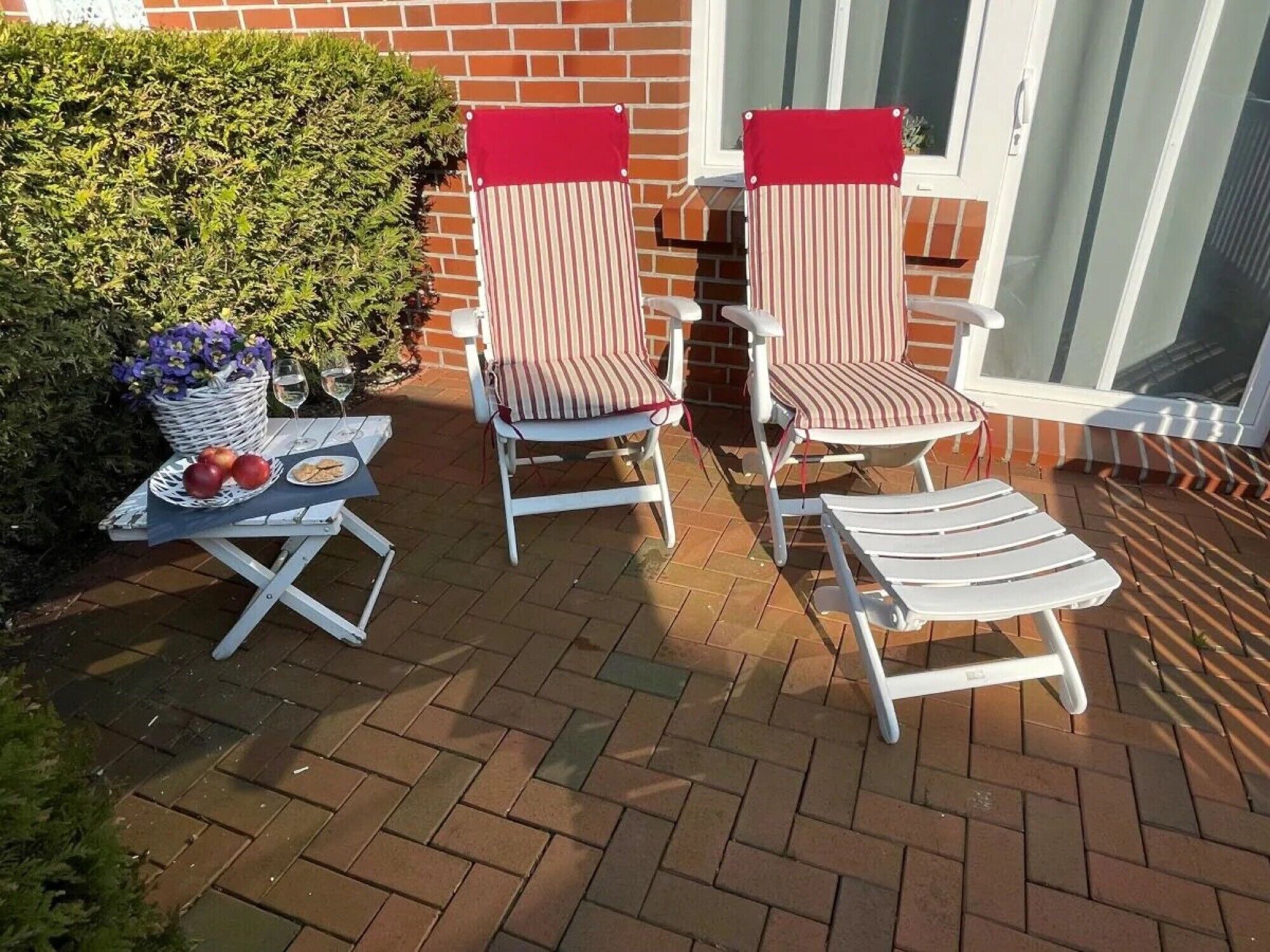 Eine Terrasse mit zwei gestreiften Liegestühlen, einem Tisch mit einer Blumenkorb und einem Weinglas.