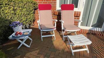 Eine Terrasse mit zwei gestreiften Liegestühlen, einem Tisch mit einer Blumenkorb und einem Weinglas.