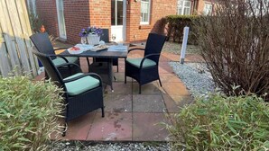 Un patio al aire libre con una mesa lista para dos personas, rodeado de sillas de mimbre con cojines.