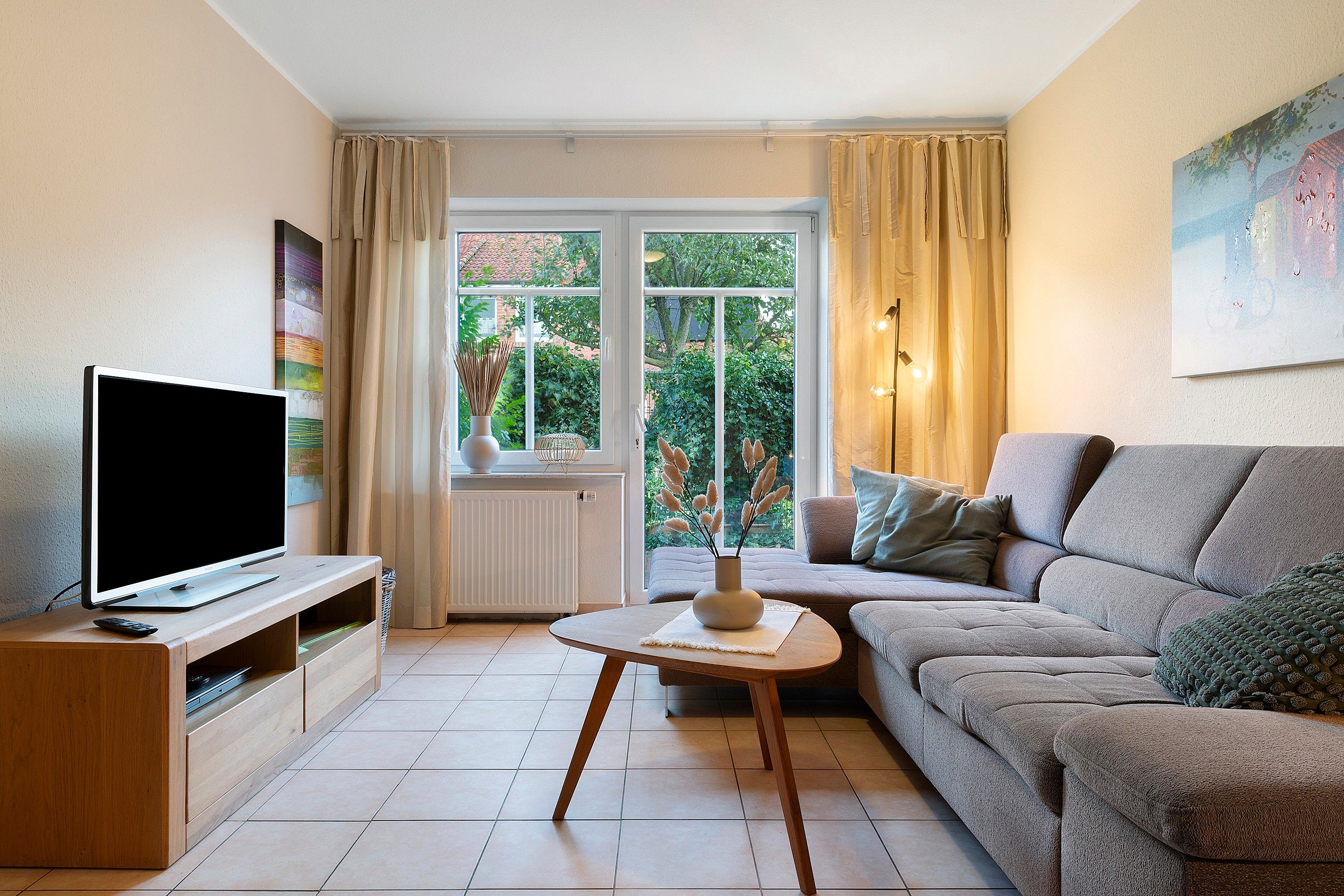 Una sala de estar con televisor, sofá y ventana con cortinas.