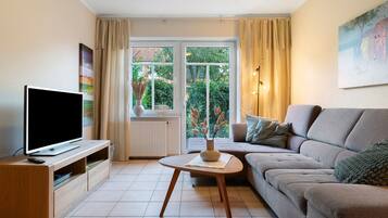 Una sala de estar con televisor, sofá y ventana con cortinas.