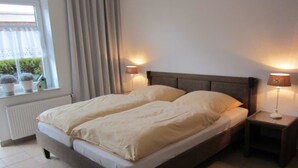 Una cama doble con cabecera de madera, dos lámparas de noche, una ventana con cortinas y un radiador.