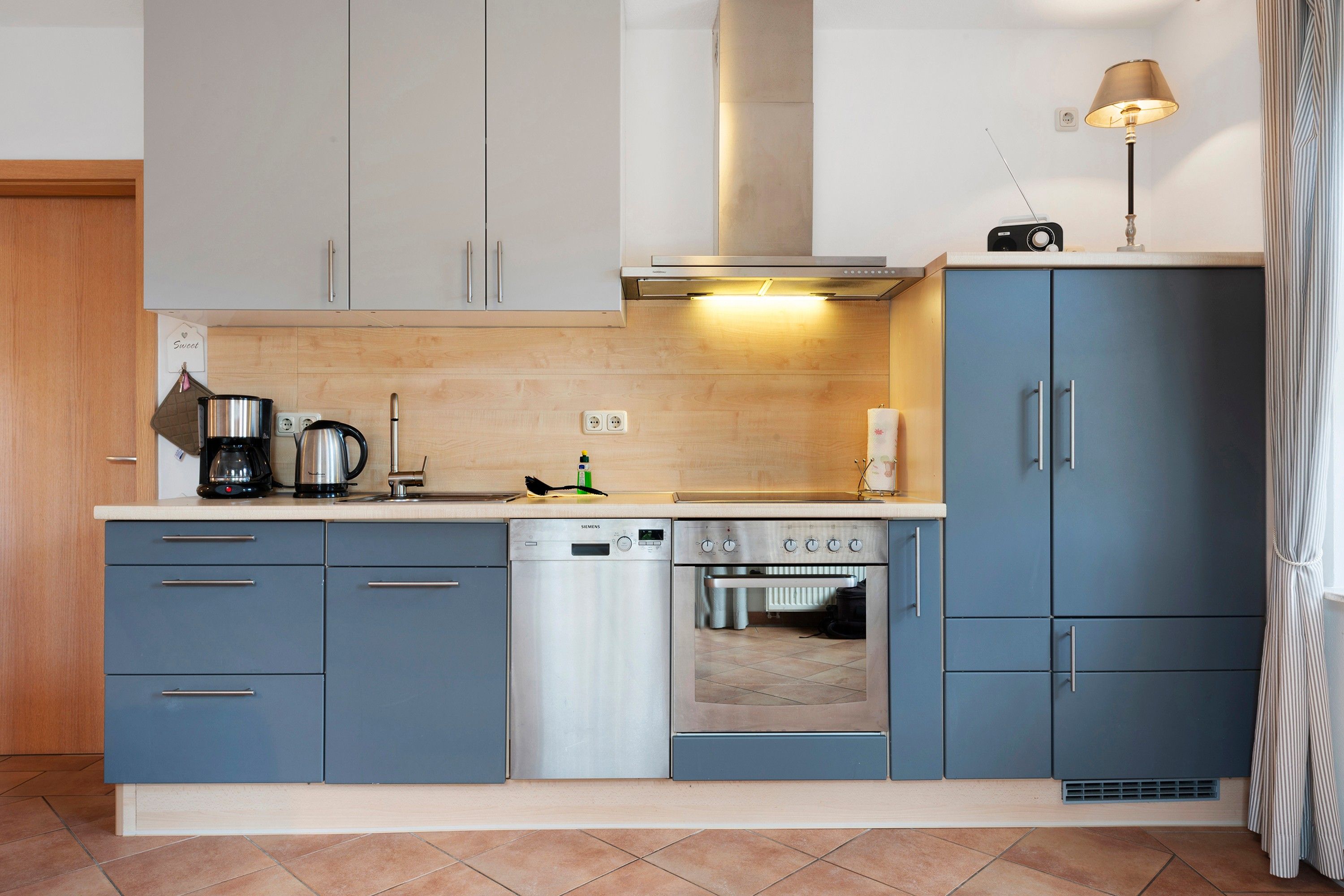 Une cuisine moderne avec des meubles gris, un lave-vaisselle, une cuisinière et une machine à café.
