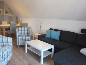 A living room with a sofa, armchair, and a coffee table. There is a desk with a chair and a lamp.