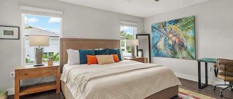 Un dormitorio con cama, escritorio, silla, ventilador de techo y una obra de arte en la pared.