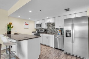 A modern kitchen with stainless steel appliances, a granite countertop, and a central island with bar stools. - Holiday Villas III #709 (Indian Shores)