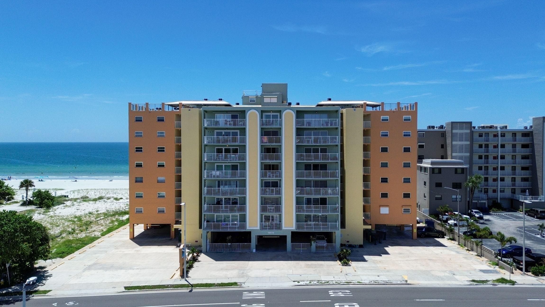 A multi-story hotel with a central courtyard, located near a beach with a clear view of the ocean.