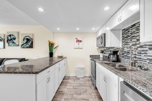Une cuisine moderne dotée de plans de travail en granit, de meubles blancs, d’un évier en acier inoxydable et d’un four à micro-ondes.