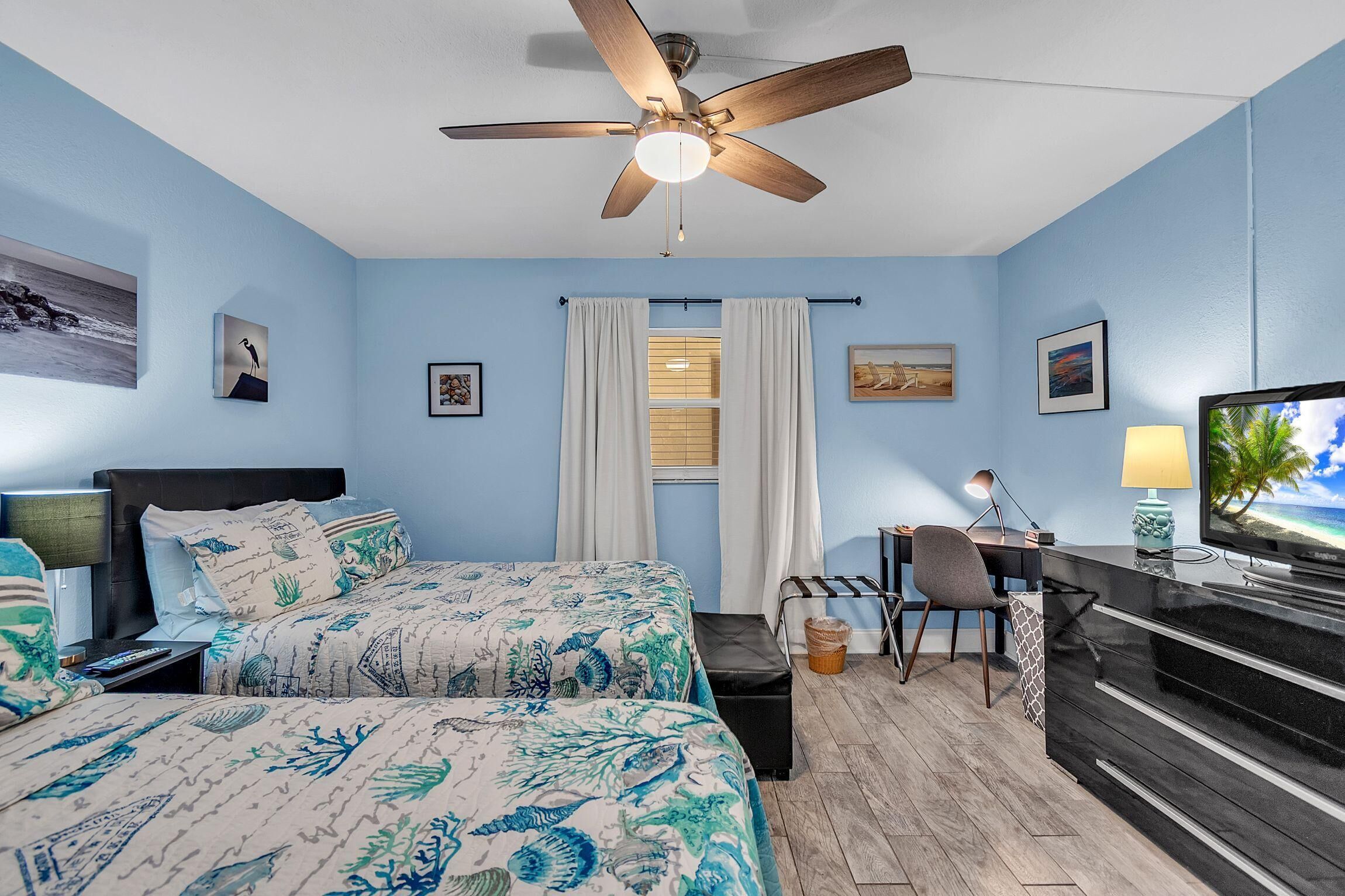 A bedroom with a bed, a desk, a chair, a television, and a ceiling fan.