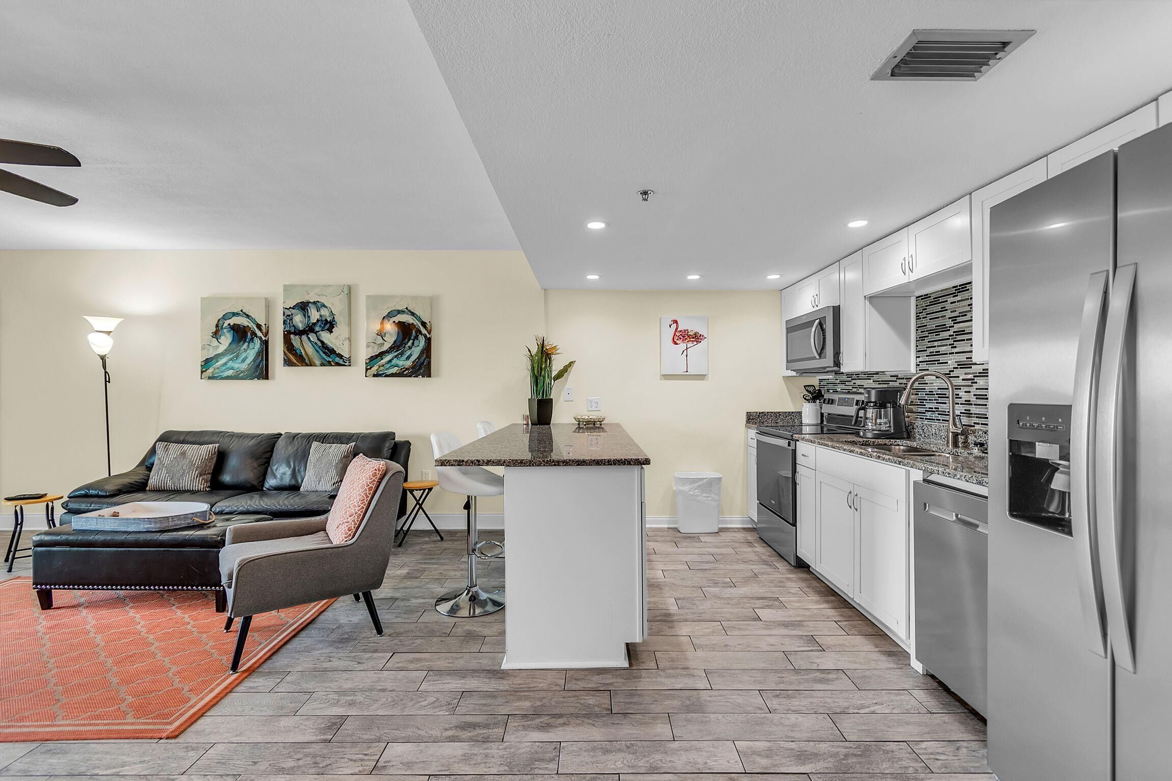 A modern kitchen with stainless steel appliances, a dining area with a sofa and coffee table, and artwork on the walls.