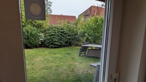 Udsigt gennem en dør til en baghave med græsplæne, et bord og stole, samt en hæk.