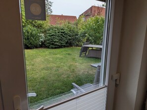 Blick durch eine Tür auf einen Hinterhof mit Rasen, einem Tisch und Stühlen sowie einer Hecke.
