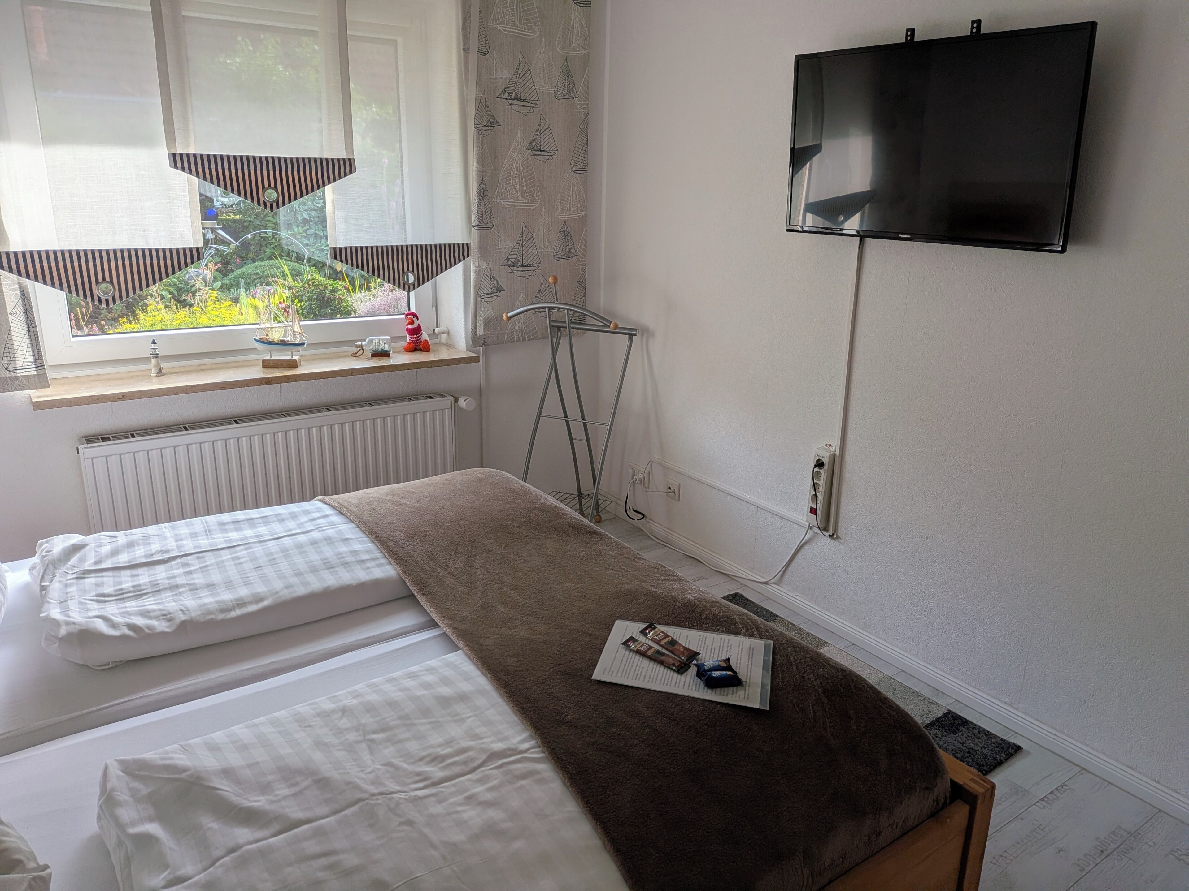 A bedroom with two beds, a window with a view, a TV mounted on the wall, and a radiator.