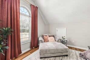 Ein Schlafzimmer mit Bett, Nachttisch, Topfpflanze und einem Fenster mit Vorhängen.