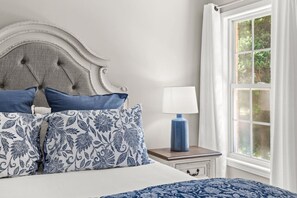 Ein Schlafzimmer mit Bett, Kissen, einem Nachttisch mit Lampe und einem Fenster mit Vorhängen.