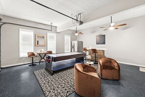Ein modernes Zimmer mit Billardtisch, zwei Ledersesseln, Deckenventilator und einem gemusterten Teppich.