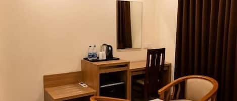 Una habitación pequeña con escritorio, dos sillas, un espejo, una ventana con cortinas y un ventilador de techo.
