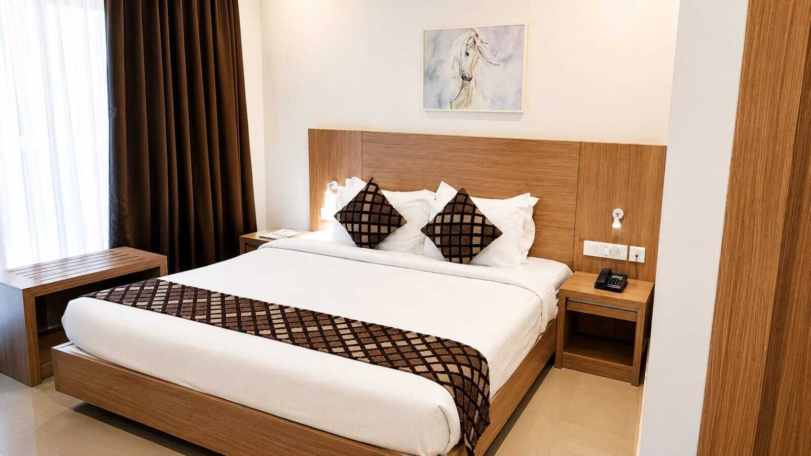 A hotel room with a large bed, two bedside tables, a nightstand, a wall-mounted phone, and a painting above the bed.