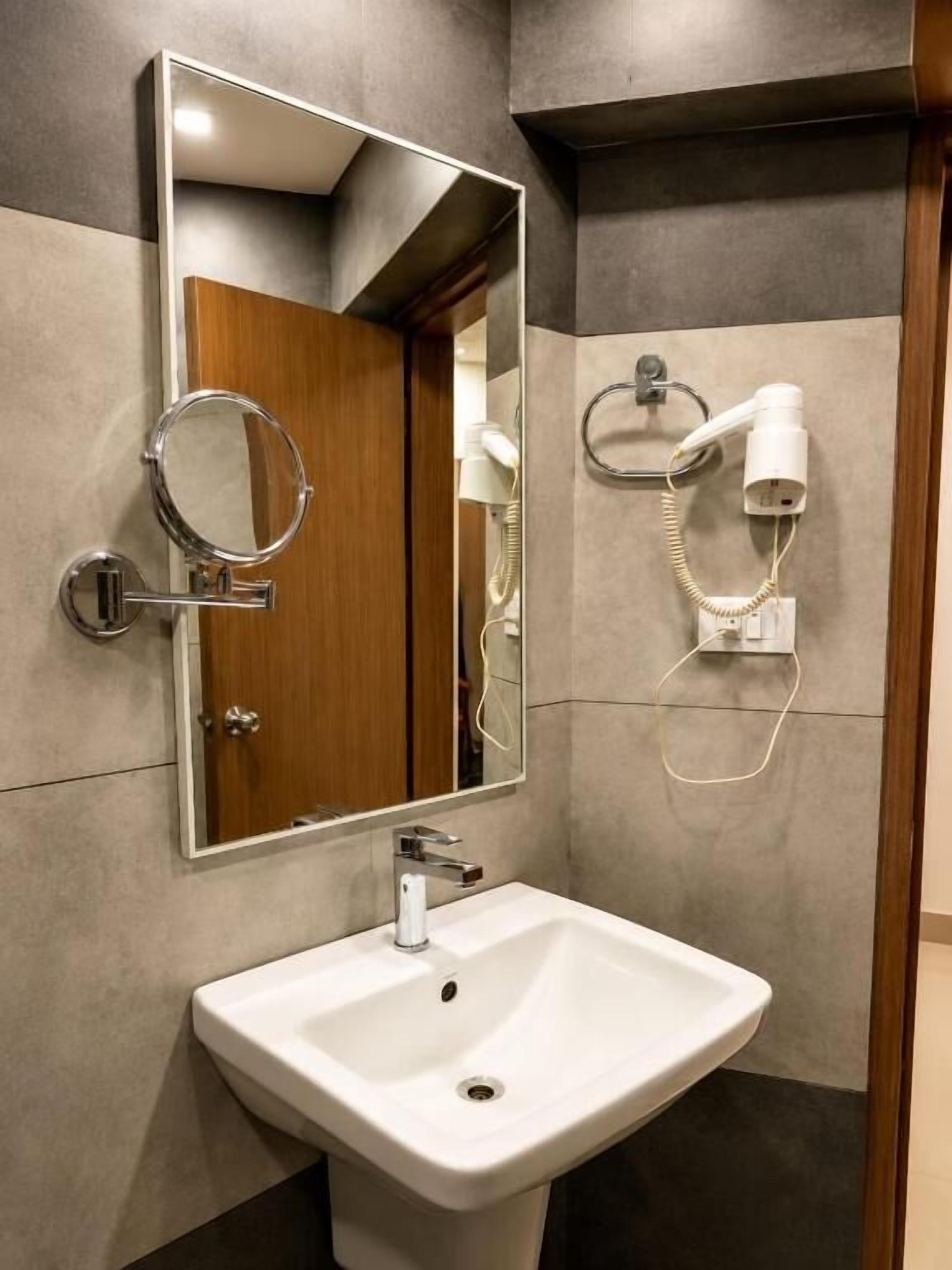 A bathroom with a white sink, a mirror, and a hairdryer mounted on the wall.