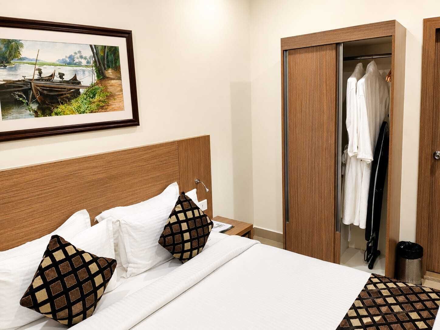 A hotel room with a bed, pillows, a wardrobe, and a framed picture on the wall.
