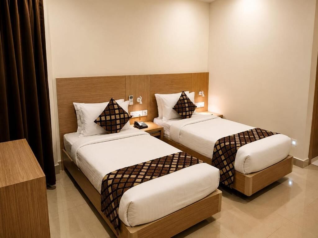Habitación de hotel con dos camas, cada una con cabecero de madera, ropa de cama blanca y una manta a cuadros. Se observa una mesita de noche con una lámpara y un teléfono junto a una de las camas.