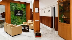 Un vestíbulo de hotel con mostrador de recepción, un zapatero y un cartel con el nombre 'Sakthi'.