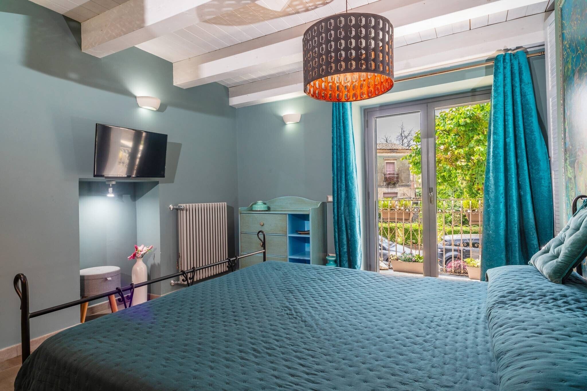 Een slaapkamer met een bed, een televisie, een radiator, een raam met gordijnen, en uitzicht op de omgeving.
