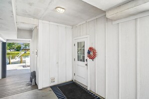 Een witte deur met een ruit en een krans, een houten terras en een boot afgemeerd.