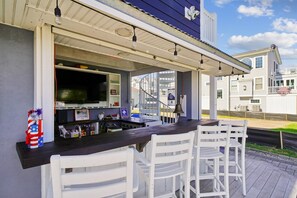 Ein Außenbereich mit Bar, einer Theke, weißen Stühlen und einem Fernseher.