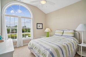 Una camera da letto con una grande finestra, un letto con lenzuola a righe, un comodino con una lampada e un quadro appeso al muro.