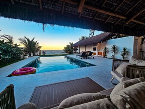 A pool area with a view of the ocean, lounge chairs, and a thatched-roof structure. - Casa Geller (Ipojuca)