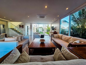 A modern living room with a sofa set, a coffee table, and a TV. There is a staircase leading to another level. - Casa Geller (Ipojuca)