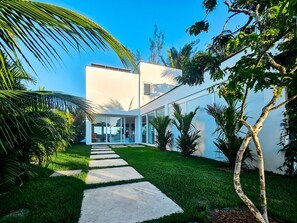 A modern building with a glass facade, a paved walkway, and lush greenery. - Casa Geller (Ipojuca)