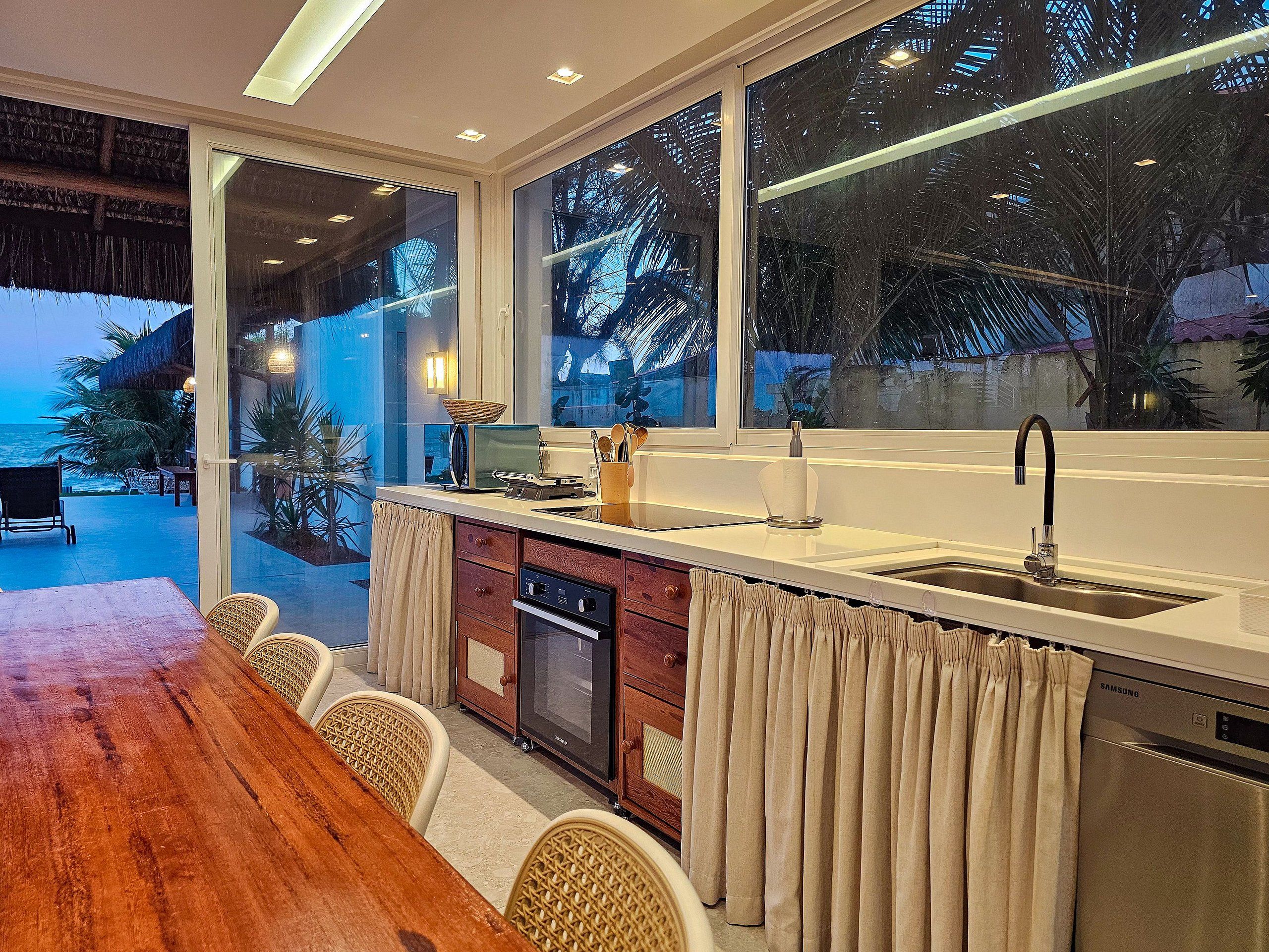 Eine moderne Küche mit einem großen Fenster, einem Essbereich mit Holztisch und Blick aufs Meer.