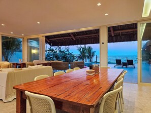A dining area with a wooden table and chairs, a sofa, and a view of the ocean. - Casa Geller (Ipojuca)