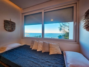 A bedroom with a bed, a window with a view of the sea, and a wall decoration. - Casa Geller (Ipojuca)