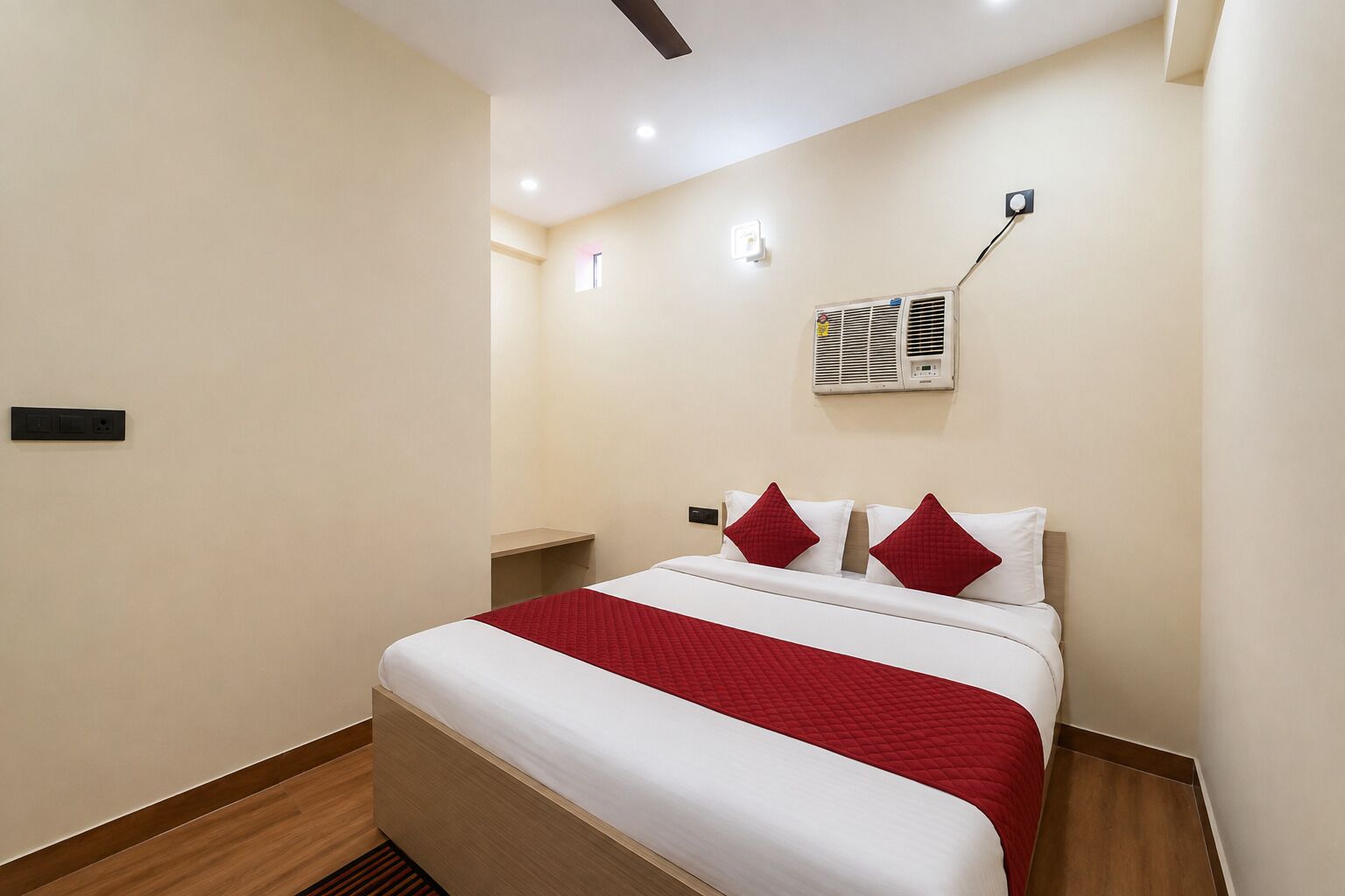 Una habitación de hotel con cama, mesita de noche, aire acondicionado y una lámpara fijada a la pared.