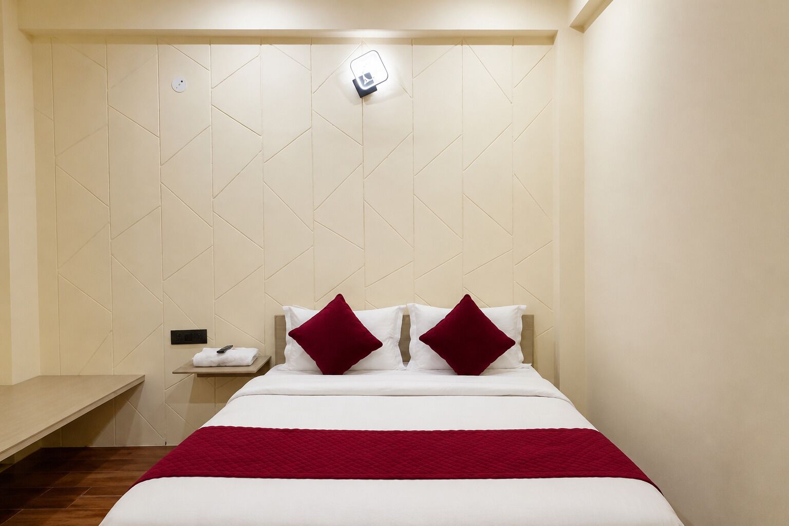 Una habitación de hotel con una cama, una mesita de noche y una lámpara fijada a la pared.