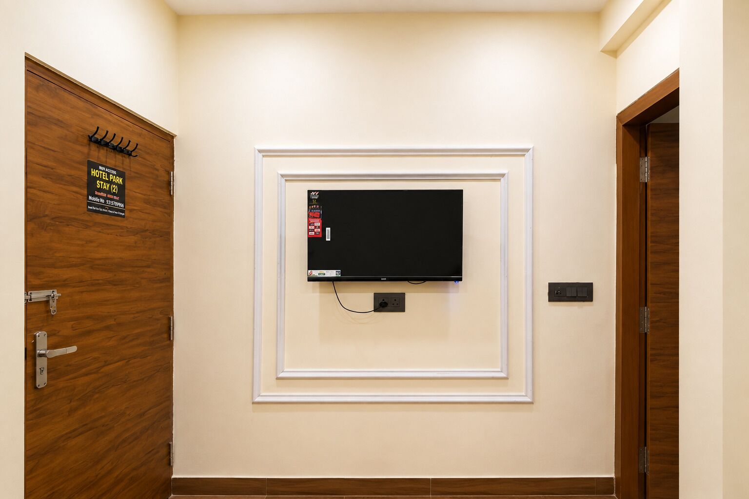 Habitación de hotel con televisión montada en la pared, puerta de madera con un cartel y un interruptor de luz también fijado a la pared.