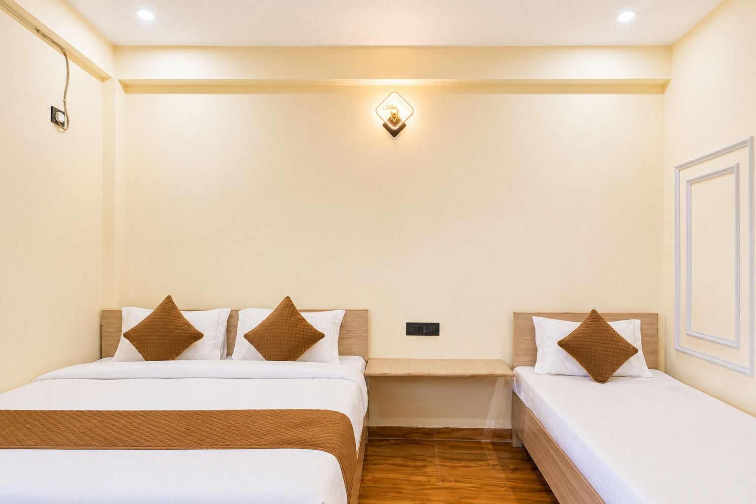 Quarto de hotel com duas camas, uma mesa de cabeceira, uma luminária na parede e uma tomada.