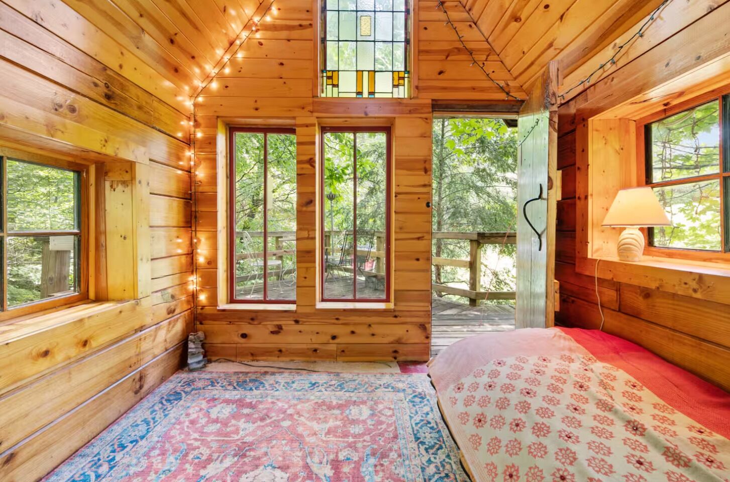 A wooden cabin interior with a bed, a rug, and a window with a view of the outdoors.