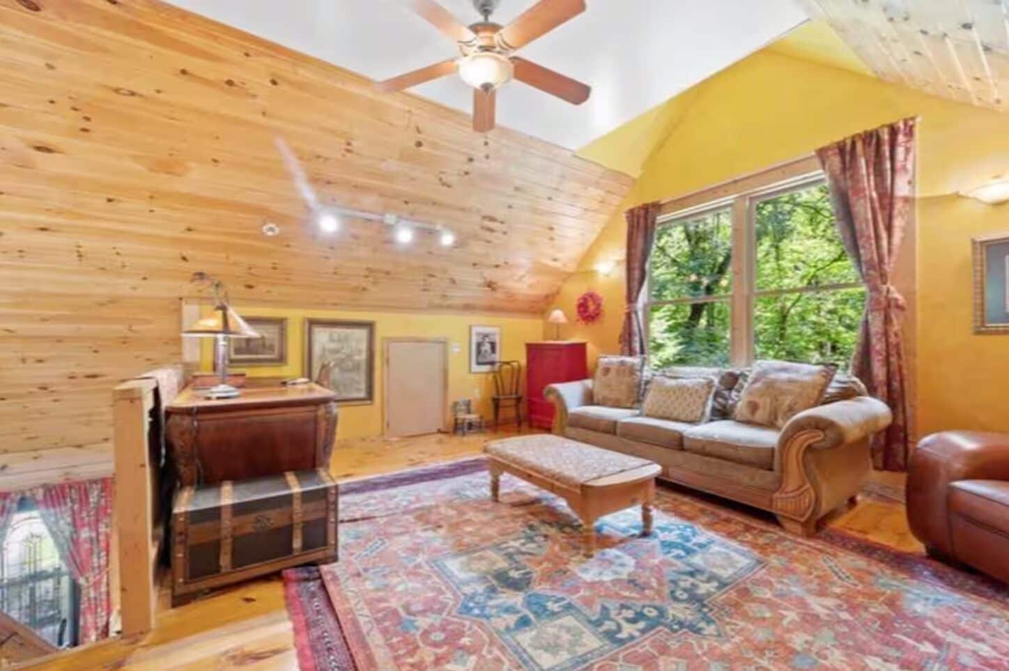 A cozy living room with a wooden ceiling, a sofa set, a coffee table, and a large window with curtains.