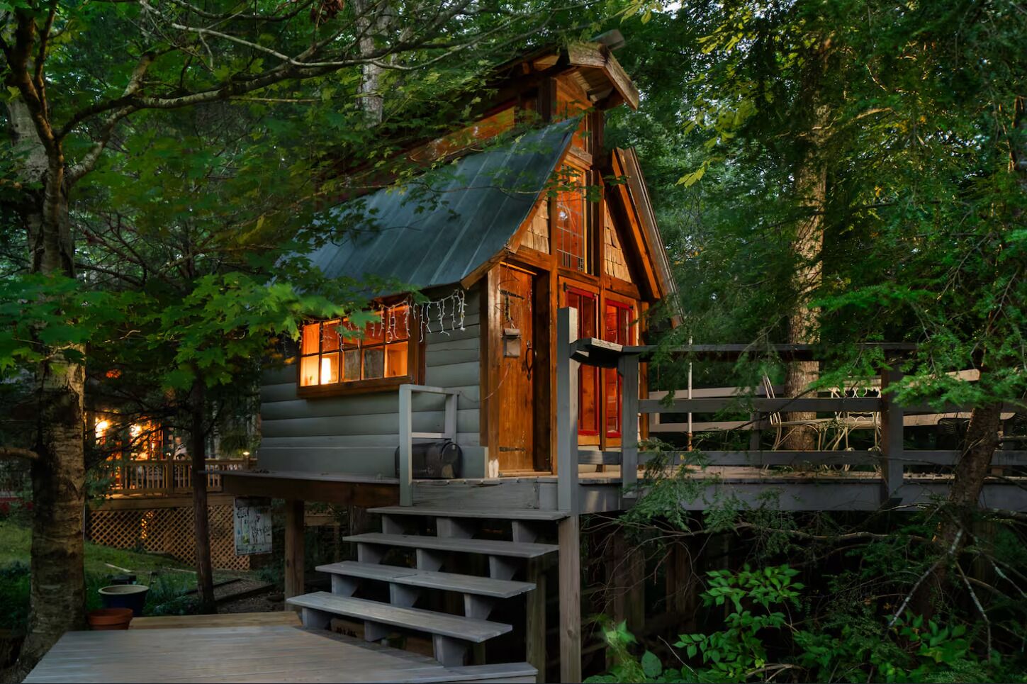 A wooden cabin with a metal roof, surrounded by trees and a wooden deck.